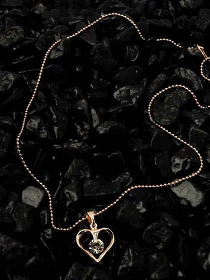 A heart-shaped pendant necklace photographed against a bed of black stones. The dark, textured background makes the rose gold pendant stand out dramatically.