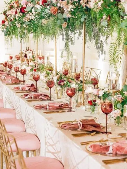 An elegant long table setup for a wedding reception, featuring blush pink chairs and dramatic, elevated floral arrangements. This style of seating is perfect for creating a communal and intimate dining experience, even at a large event.