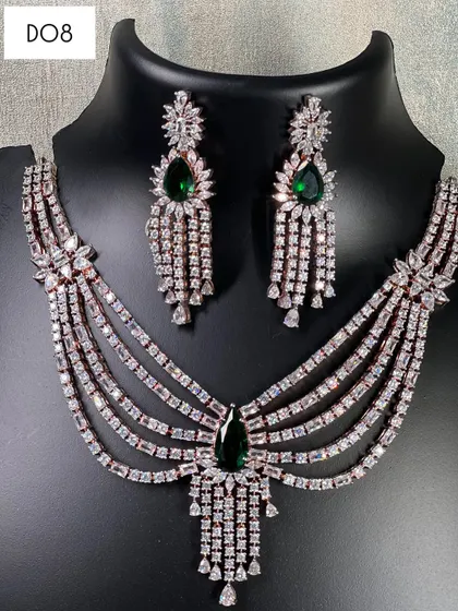 This multi-layered necklace in a rose gold finish features emerald green stones and a dramatic pendant. It's a bold rental choice that combines modern trends with classic glamour.