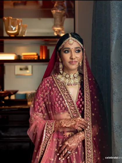 This portrait showcases the complete traditional bridal look. The makeup is balanced to harmonize with the deep maroon lehenga and heavy jewelry, creating a cohesive and regal appearance.
