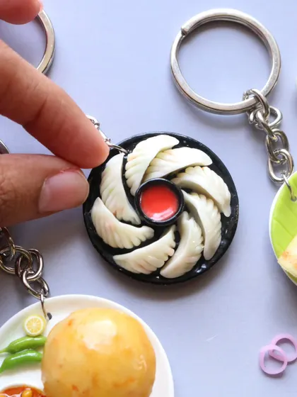 A close-up of a momo keychain, showing the delicate folds of the dumplings and the tiny bowl of dipping sauce.