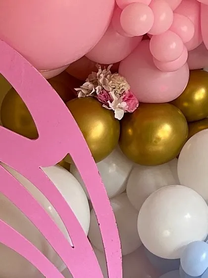 A detail shot of a balloon garland, showing a mix of pink, gold, and white balloons accented with small flowers and a large pink butterfly wing prop.