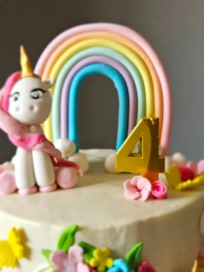A close-up of the unicorn and rainbow cake, focusing on the sweet, handcrafted unicorn figurine. The pastel rainbow behind it adds a perfect touch of magic.