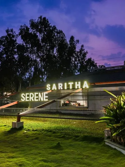The marketing office for Saritha Serene, seen here at dusk. The illuminated signage and landscape lighting transform the building into a beacon, highlighting its unique architectural form against the evening sky.