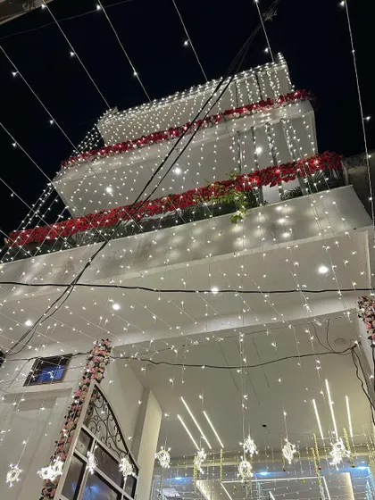 A beautiful white house decorated for a wedding. The balconies are adorned with red flowers, and the facade is draped in strings of fairy lights.