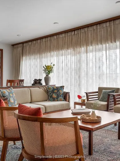 For the 'Gulmohar' home, we created a linear arrangement for the living and dining areas to maximize the balcony view. A custom crockery unit acts as a subtle divider, while ceiling-to-floor curtains soften the space and enhance its cozy feel.