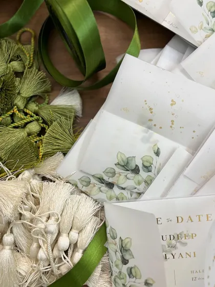 A behind-the-scenes look at the elements for our Save the Date cards, including stacks of vellum wraps, green ribbons, and piles of custom-made tassels.