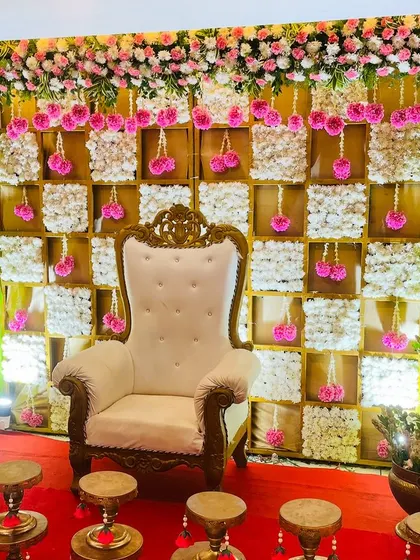 A beautiful pink and white themed backdrop for a baby shower. The checkerboard design is made with panels of white flowers, accented by hanging pink floral tassels for a delicate and feminine touch.