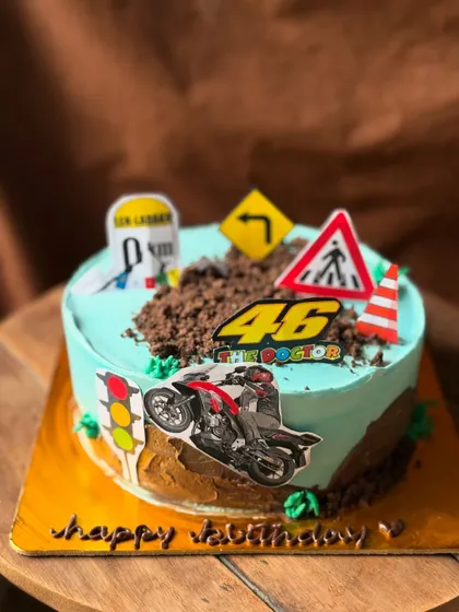 A non-fondant cake for a bike lover, featuring road signs and a motorcycle topper on a bed of chocolate "dirt".