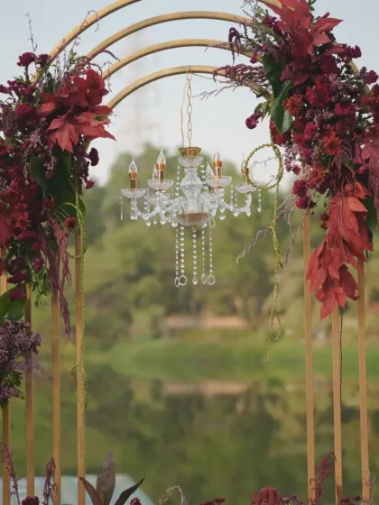 A close-up of one of the golden arches, showing the detail of the cascading red floral arrangement and the delicate crystal chandelier.