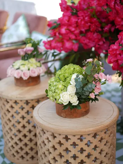 A close-up of the delicate floral arrangements in rustic wooden pots, placed on intricately carved side tables.