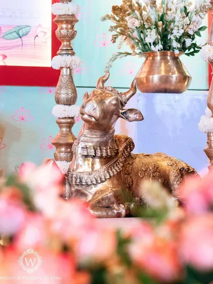 Traditional brass elements like the Nandi statue and tall diyas (lamps) are central to our South Indian decor. They are surrounded by fresh flowers, adding a touch of divinity and cultural richness.