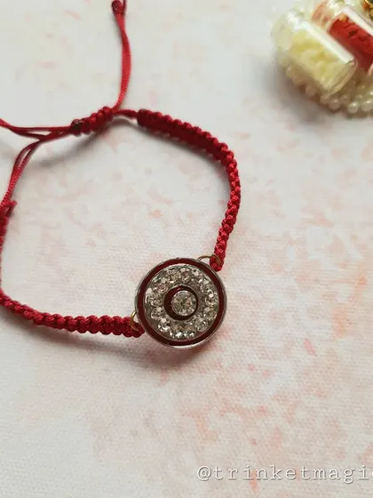 The red crystal Rakhi, shown here with its Roli-Chawal holder. The braided red thread is adjustable and comfortable to wear.