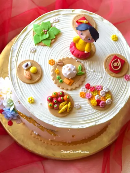 A top-down view of the Rice Ceremony cake, showing the intricate, hand-crafted details of the baby figure, food items, and other symbolic elements.