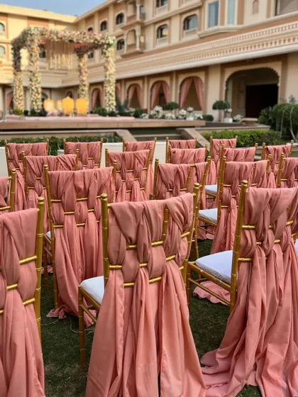 Elegant chair decor with coral peach drapes, tied with golden rings to match the overall theme of the wedding.