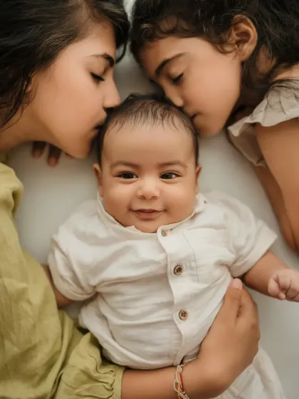 An overhead shot of two sisters kissing their baby brother's head. A sweet and artistic way to capture a sibling portrait.