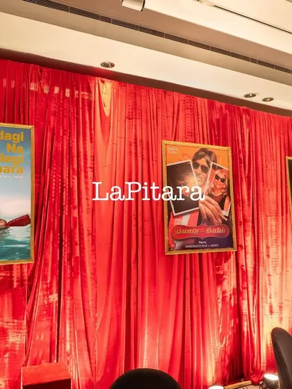 A wall draped in dramatic red velvet, adorned with custom-made posters of the birthday person inserted into classic Bollywood movie posters.