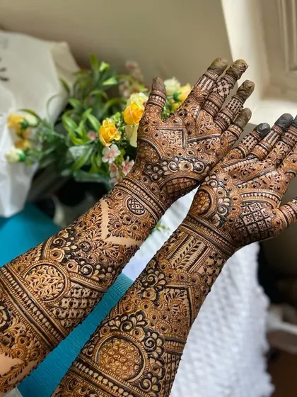 Full bridal mehendi for both hands, showcasing symmetrical patterns that extend up the forearms. The design is packed with detail, including mandalas, paisleys, and fine-line fillers.