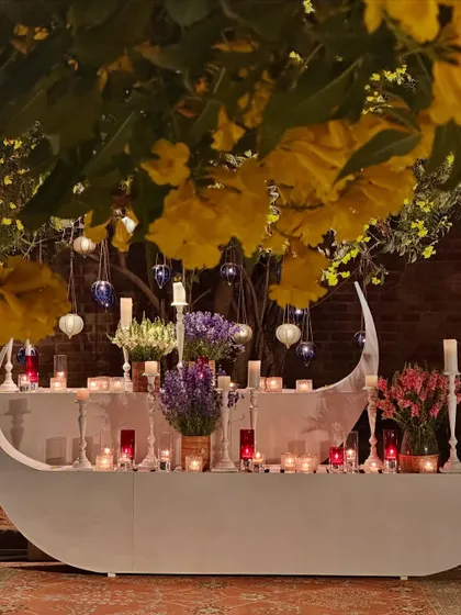 The same tree, now transformed into a romantic "boat" table with candles and colorful flowers, under a canopy of yellow blooms.