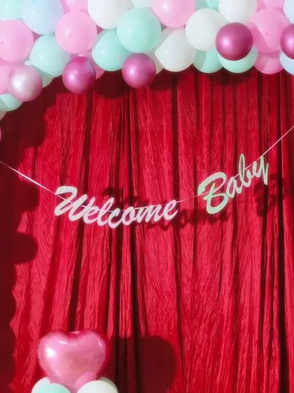 A close-up of a "Welcome Baby" banner against a rich red curtain. The simple white lettering stands out beautifully, creating an elegant focal point.