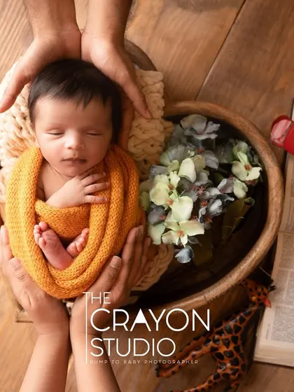 A newborn sleeps in a wooden bowl, cradled by his parents' hands. This overhead shot emphasizes the feeling of being cherished and protected.