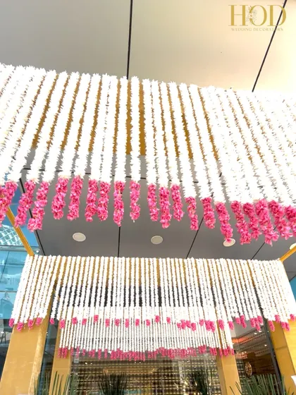 Looking up at the ceiling of the entrance, covered in layers of white and pink floral strings. This detail shows the density and richness of the floral work required to create such a luxurious effect.