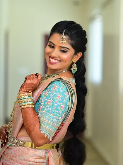 A happy bride smiling, wearing a beautiful light blue blouse with delicate pink and white floral embroidery.
