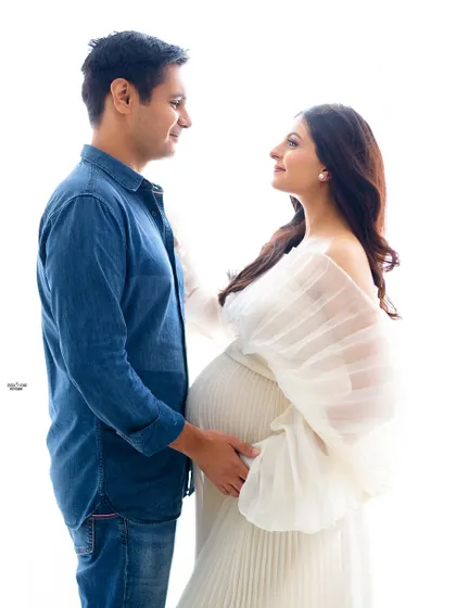 A lovely high-key portrait of a couple ready to welcome their new baby. The flowing white gown and the partner's casual denim shirt create a relaxed and happy vibe.