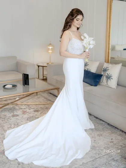 A full-length shot of the bride in her elegant white mermaid gown, holding a bouquet of white lilies, looking serene and beautiful.