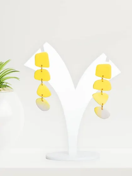 Bright yellow tiered earrings styled with a small plant to add a touch of life and color. This simple styling elevates a standard e-commerce shot.