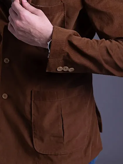 A close-up of a brown corduroy jacket, showing the sleeve buttons and patch pocket. Unlock your personal style with bespoke pieces that fit your unique taste.