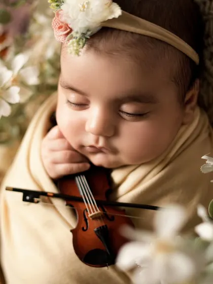 A close-up shot of the newborn with the violin. This detailed view shows her tiny hand resting near the instrument, a truly artistic and unique portrait.
