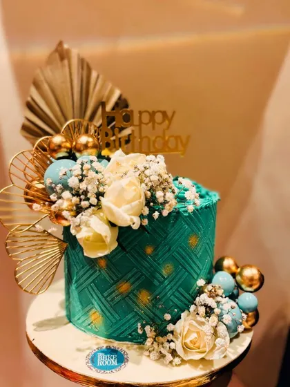 An elegant and modern cake in a beautiful sage green. The cake features a basketweave texture and is adorned with gold fans, white roses, and delicate baby's breath.