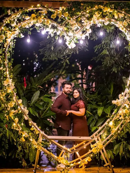 A full view of the heart-shaped arch, beautifully lit against the night sky. The couple stands inside, perfectly framed by this symbol of their love.