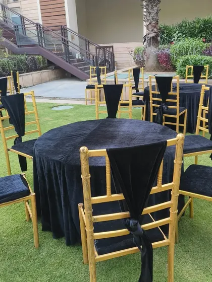 An elegant black and gold theme for event seating. The round tables are covered with black velvet, and the gold chairs are accented with black drapes for a very formal and chic look.