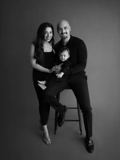 A classic black and white family portrait. The simple grey background and all-black outfits create a timeless, elegant, and sophisticated look.