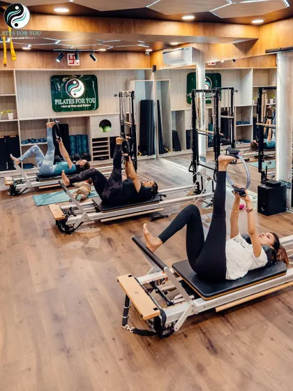 A beautiful shot of clients performing leg stretches on the Reformer. This highlights the flexibility aspect of Pilates and the calm, focused atmosphere of the studio.
