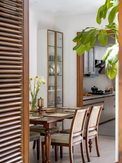 A view through a louvered wooden door into the dining room, where traditional cane chairs and a simple wooden table create a timeless aesthetic.