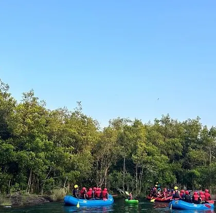 A wide, scenic view of the Kali River in Dandeli, with two rafts full of campers pausing to take in the lush green surroundings.