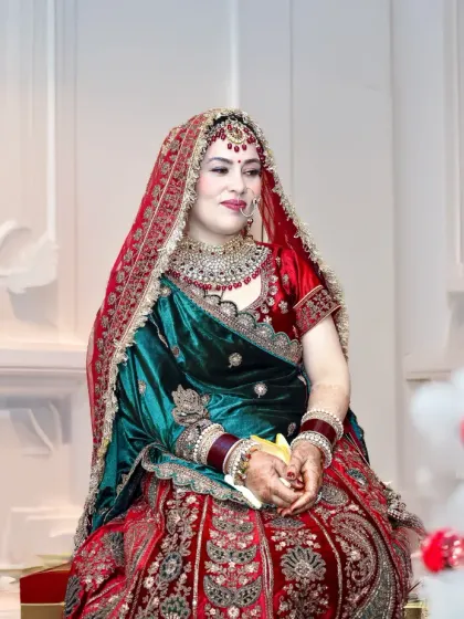 A full-length shot of the bride seated, giving a complete view of her gorgeous red and green lehenga.