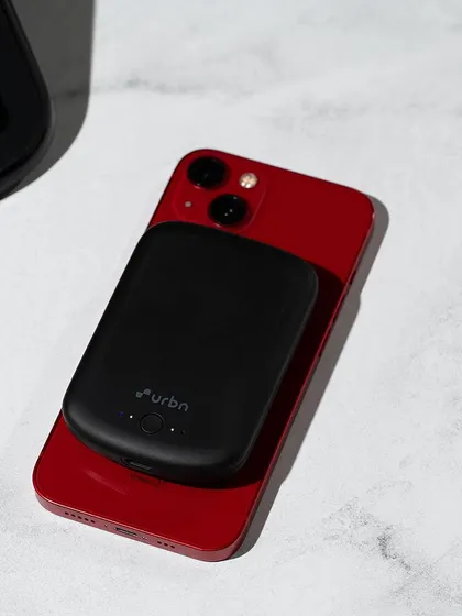 A lifestyle shot of an Urbn power bank charging an iPhone. This image demonstrates the product's use case in a realistic, everyday setting.