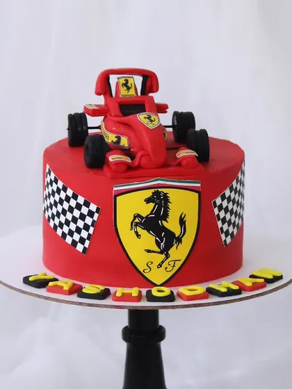 A vibrant Ferrari-themed cake for a racing enthusiast. The bold red cake is decorated with the Ferrari logo, checkered flags, and a fondant F1 race car on top.