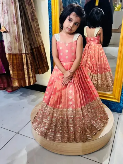 A frontal view of this gorgeous custom frock. The peach brocade fabric has a beautiful sheen, complemented by the wide, intricately woven gold border that gives it a luxurious, festive look.