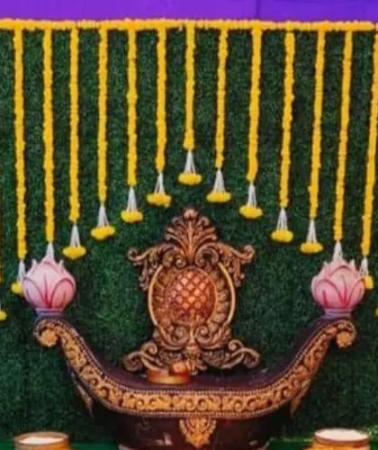 A unique cradle-like seat (jhoola) set against a greenery backdrop with hanging marigold garlands. This setup is perfect for a Haldi or Mehendi ceremony.