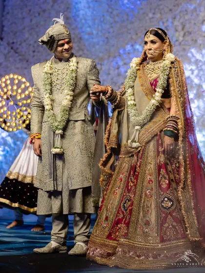 A regal wedding day look. The groom looks dashing in a custom sage green sherwani by Ankit V Kapoor, perfectly complementing the bride's magnificent multi-hued Marwar Couture lehenga.