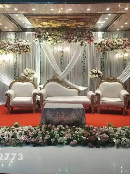 A formal reception stage with classic white furniture and soft pink floral arrangements. The design uses elegant white drapes and a clean stage front for a polished and stately appearance.