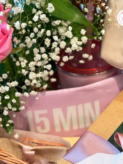 A close-up of the bride essentials hamper, showing a personalized "BRIDE" pouch and other items nestled amongst fresh flowers.