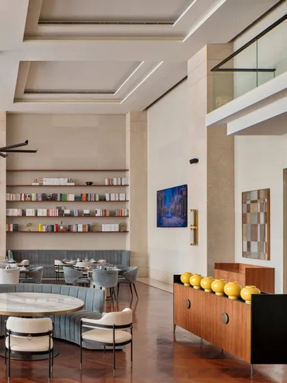 This view highlights the double-height volume of the Elevate Clubhouse living room. The open shelving, filled with curated books and objects, adds a personal, library-like feel, while the strategic placement of art and furniture defines distinct zones within the larger open plan.