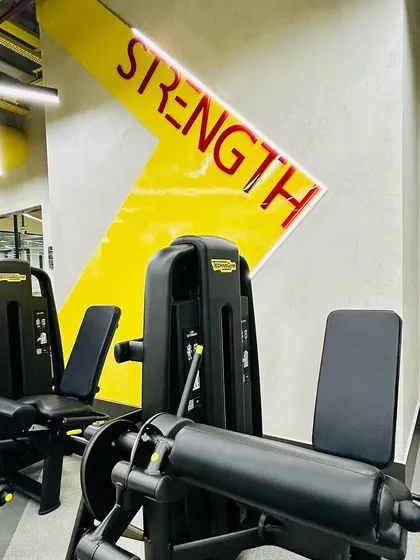 Close-up of the "STRENGTH" zone signage, which uses bold typography and the signature yellow arrow motif. This type of environmental graphic is key to navigating the space and reinforcing the gym's brand identity.