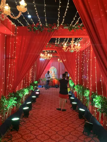 A stunning red entrance walkway for a resort wedding. The path is lined with spotlights and planters, leading through a series of draped archways with chandeliers.